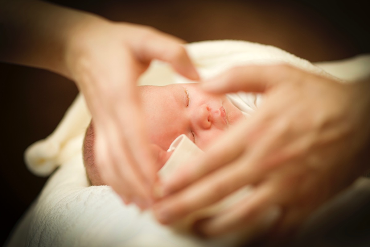 Mama und Papa formen mit ihren Hnden ein Herz und die Kamera fokussiert das dahinterliegende Babygesicht